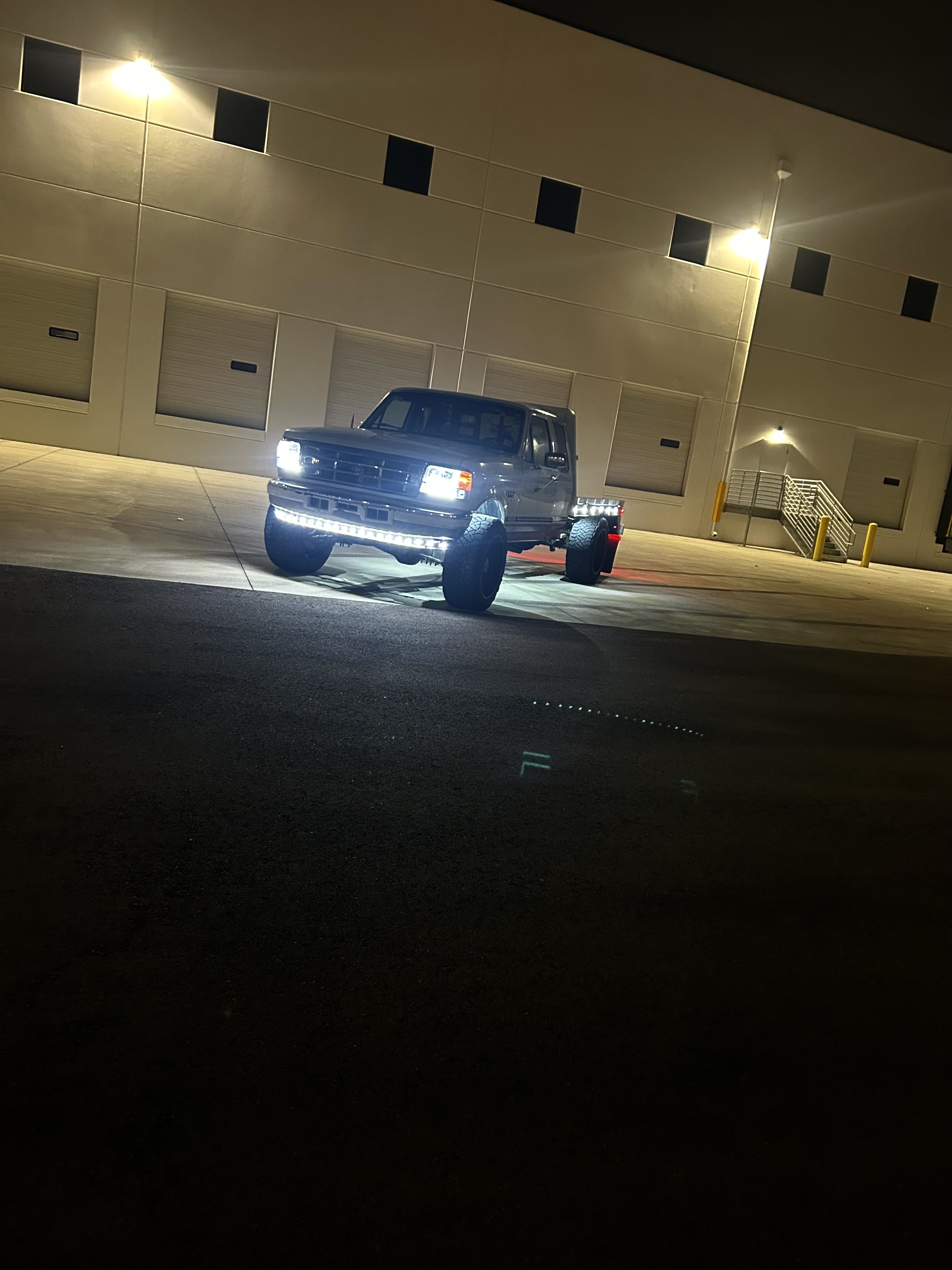 Lifted OBS Ford flatbed with custom LED bumper lighting at night